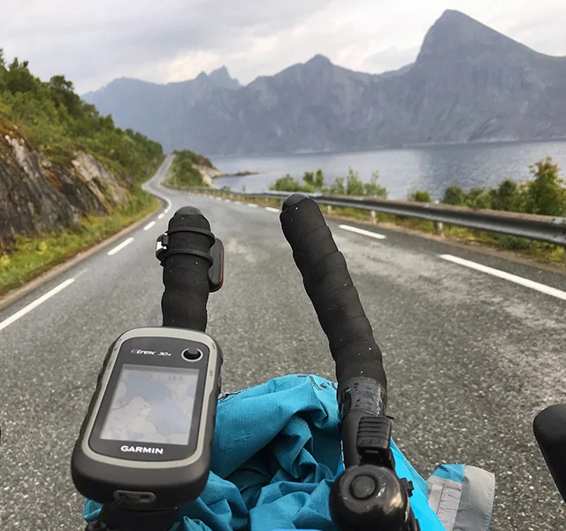 Udsigt fra person på cykel, kørende på en landevej langs vand med udsigt til bjerge